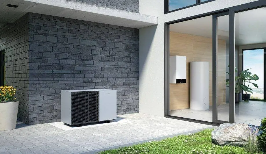 Modern patio with a heat pump unit outside a contemporary building, featuring large windows and a potted plant.