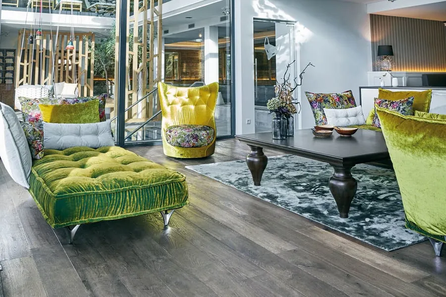 Salon moderne avec de hauts plafonds, des meubles en velours vert, des coussins floraux, un grand mur en verre et un lustre en papier blanc en cascade.