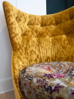 Nahaufnahme des gelben Samtstuhls mit hoher Rückenlehne und Tufting-Design "Cocoa Island", ausgestattet mit einem bunten, gemusterten Sitzkissen.