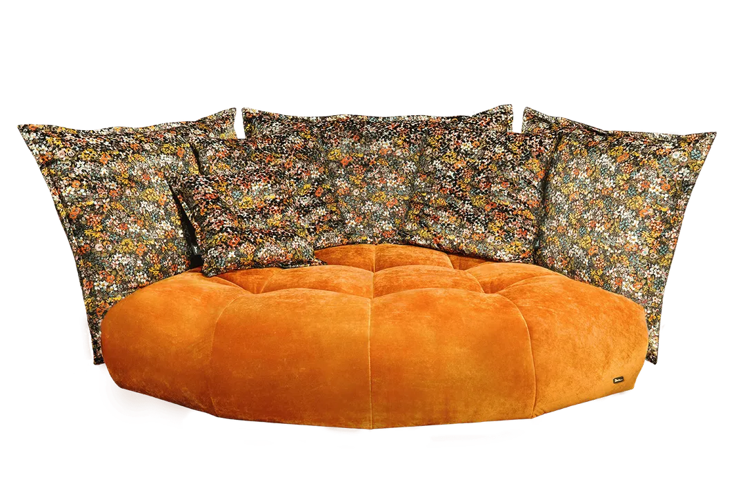 Orange plush sofa with tufted design, paired with large, colorful floral-patterned pillows.