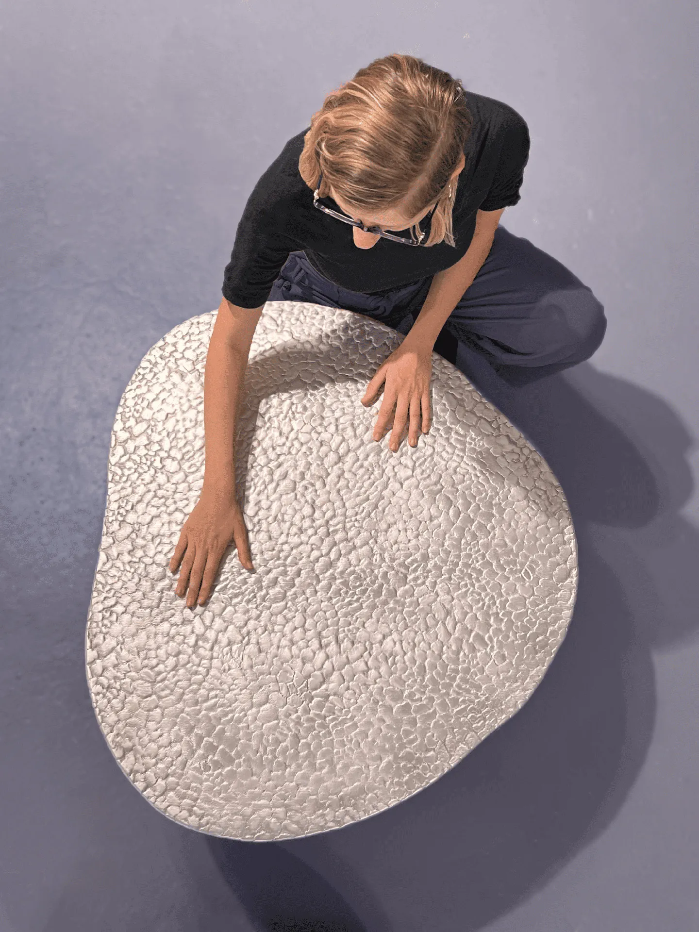 Person with glasses touching a large, textured, white stone-like object on a smooth, gray floor.