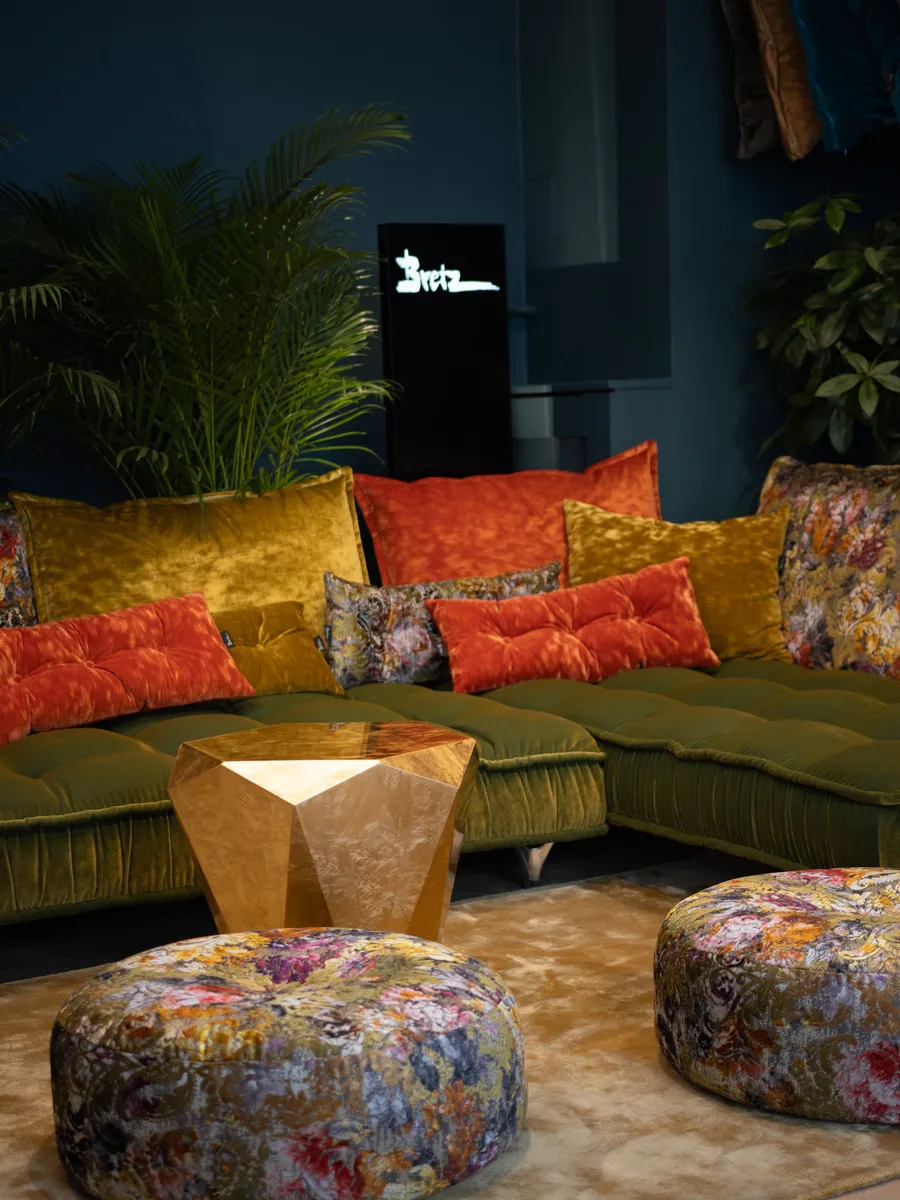 Gemütlicher Bretz Showroom mit dem Ohlinda Sofa in Oliv Grün und bunten Rückenkissen