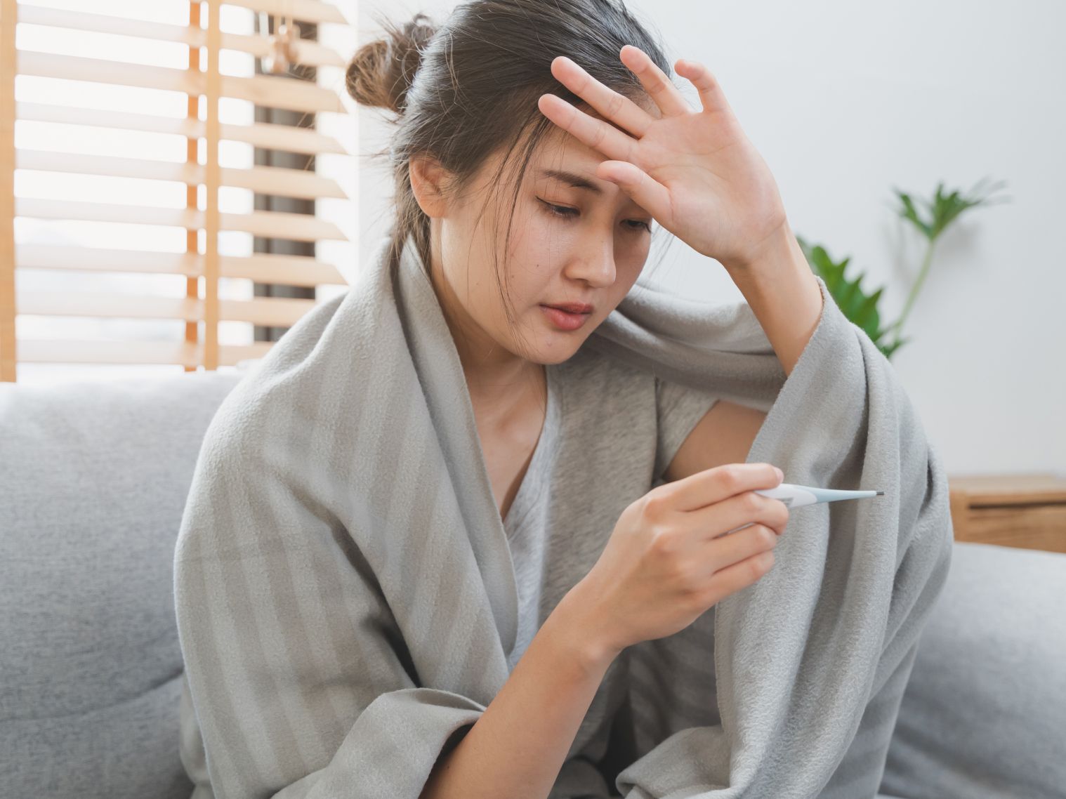 Eine Frau sitzt auf dem Sofa und misst ihr Fieber