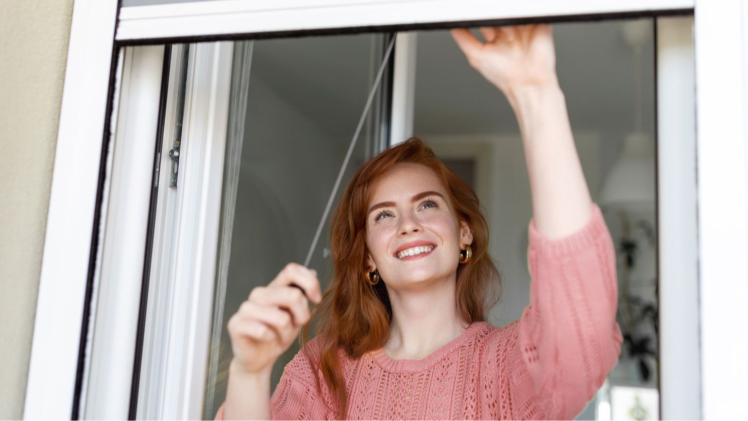 Eine lächelnde Frau steht vor einem geöffneten Fenster.