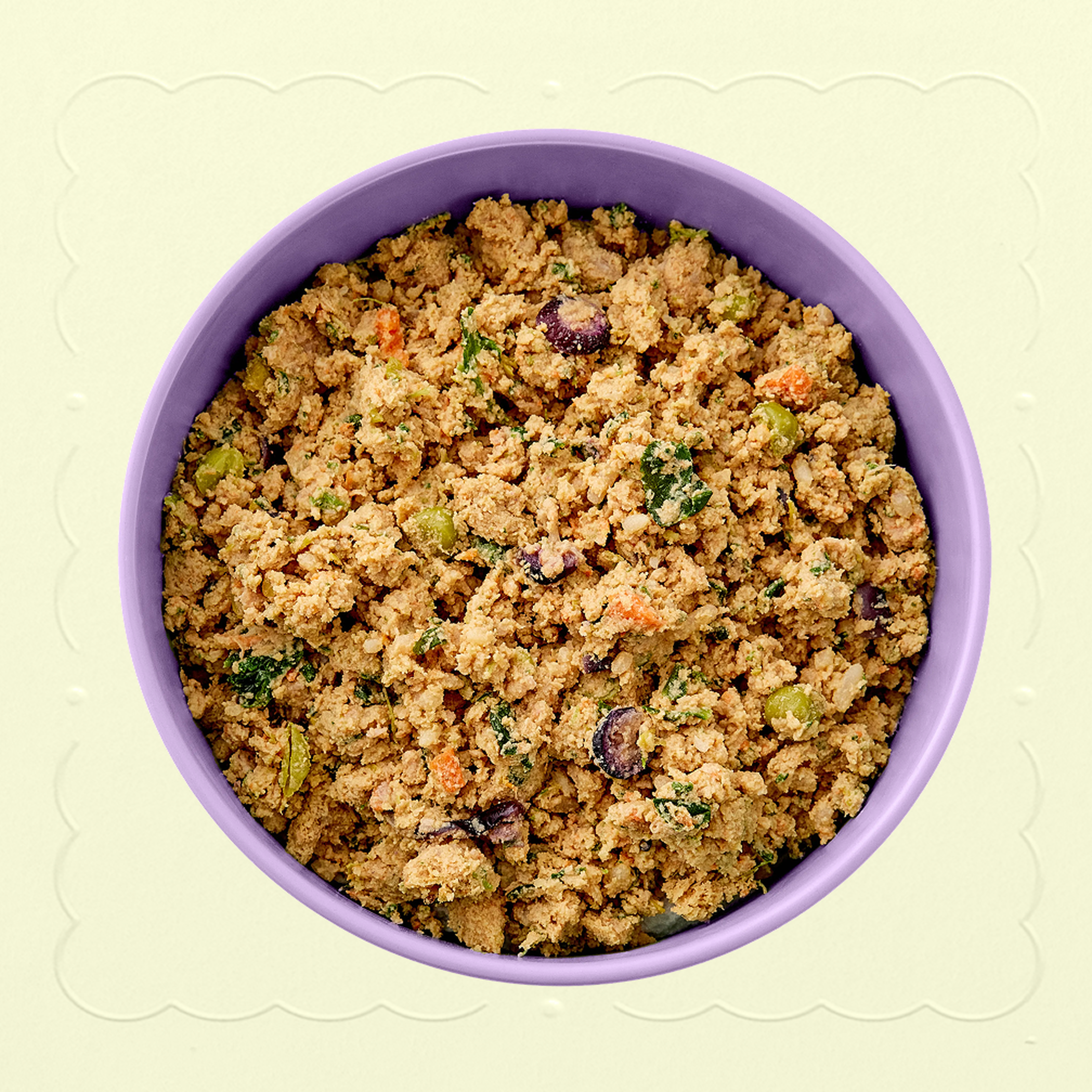 A red bowl of fPurple bowl with Fresh Chicken with Carrots Ollie recipe, with blueberry, kale, and carrot chunks visible. Bowl placed on a cream background with an embossed pattern