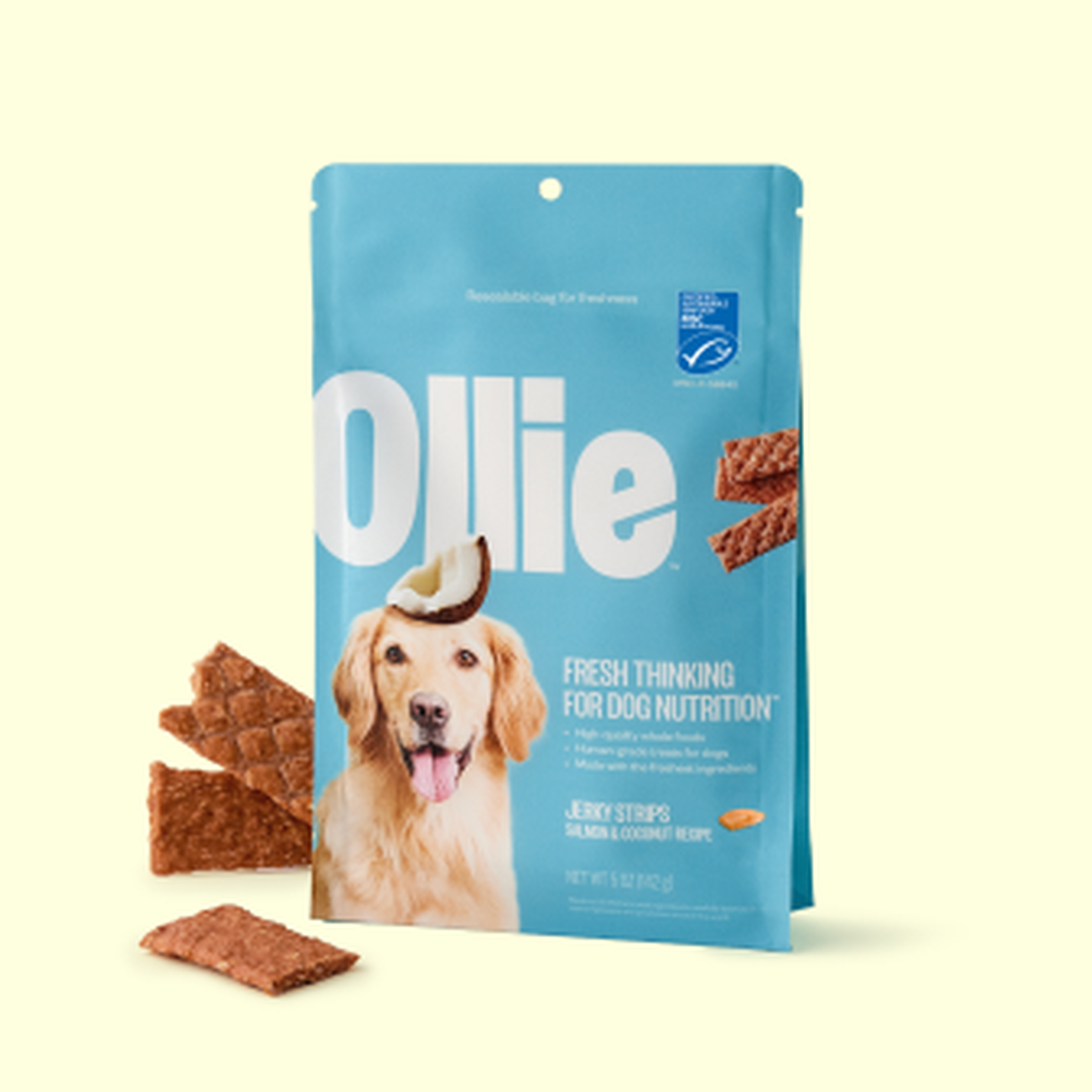 A blue bag of Ollie dog treats with a dog image on the front, surrounded by several reddish-brown treat pieces.