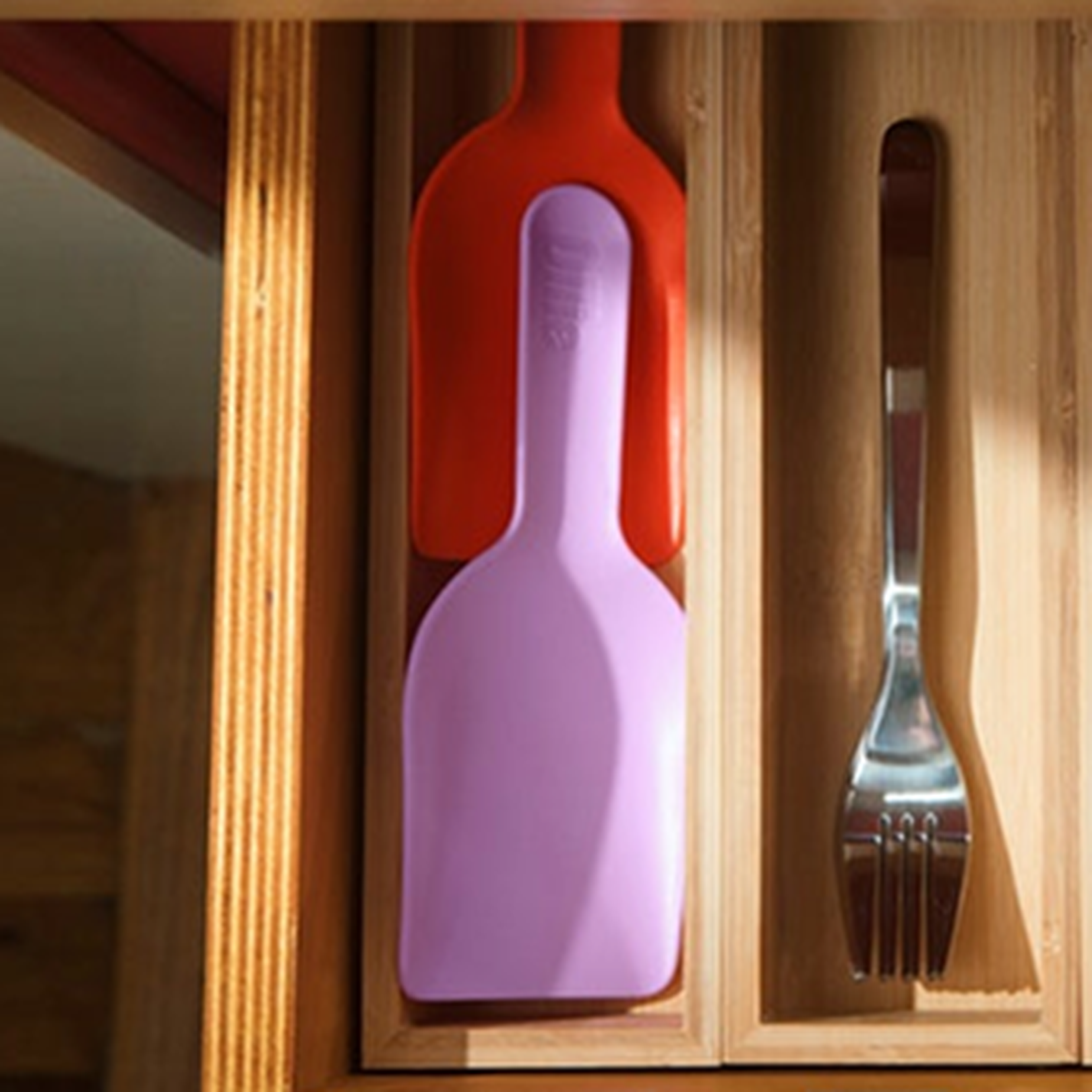 Drawer with a red and pink scoop stacked in one section and a fork in another, all in a wooden organizer.