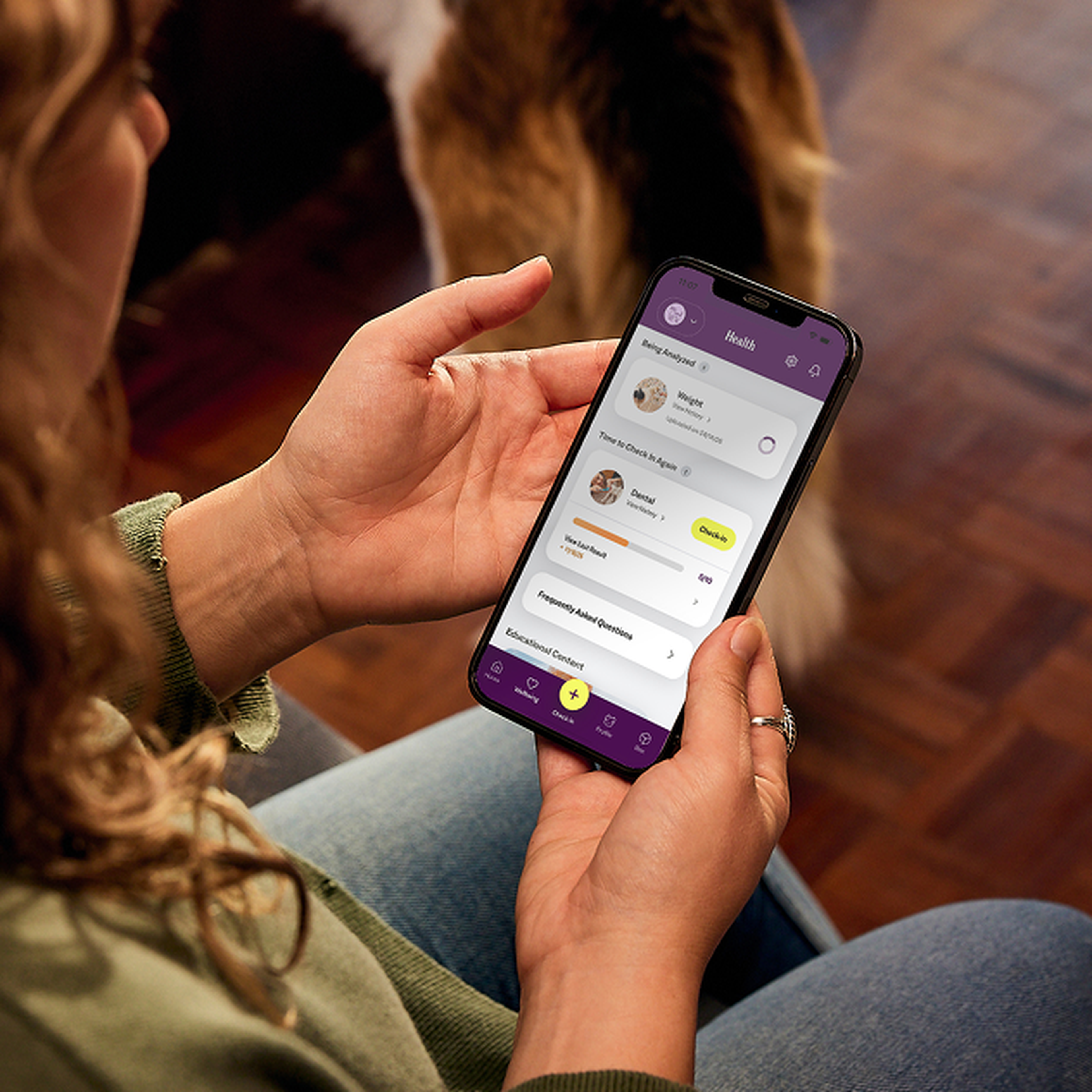 Person holding a smartphone with a health app open, displaying details like weight and daily goals. A blurred dog is visible in the background.