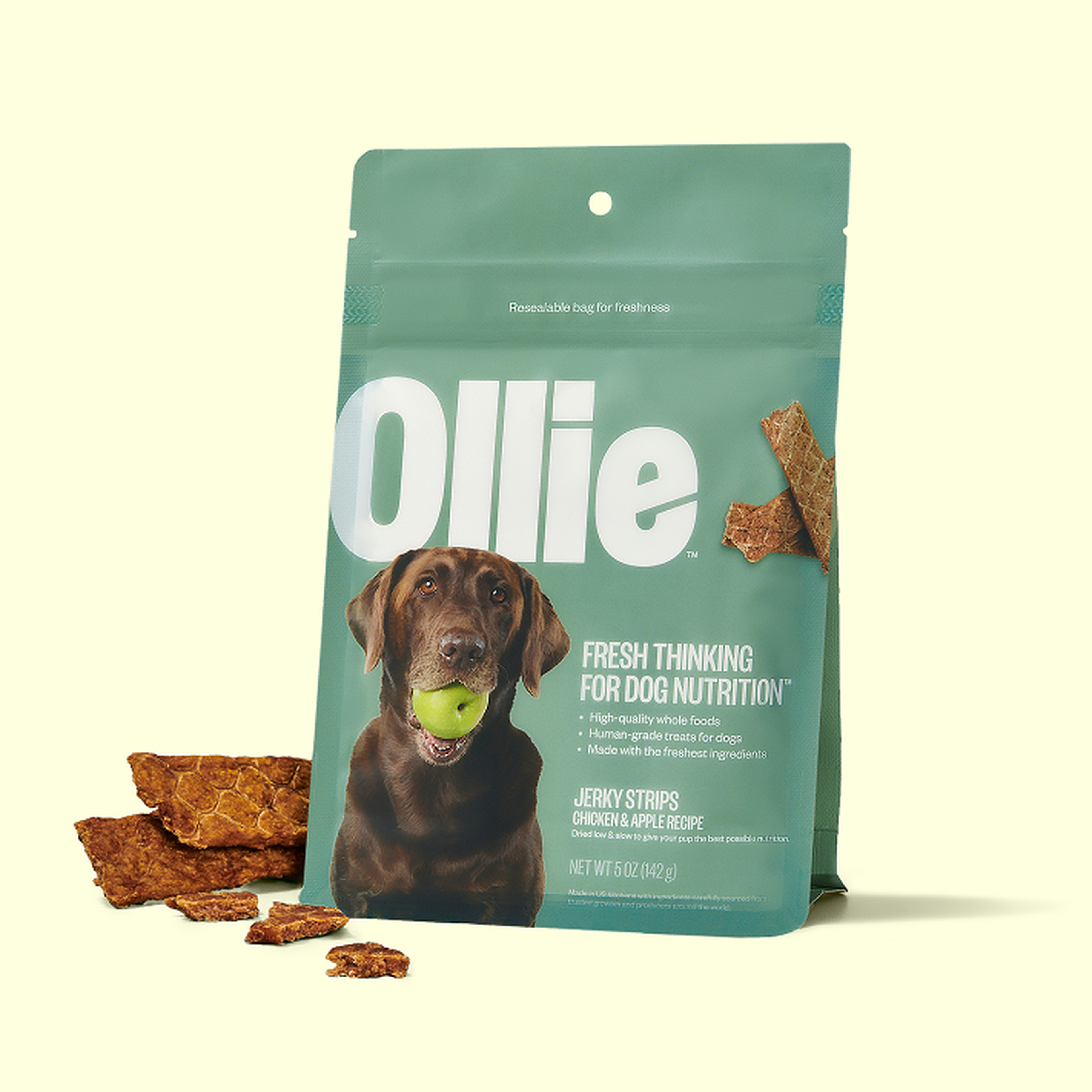 A bag of Ollie dog treats featuring jerky strips with chicken and apple recipe, depicting a dog with a tennis ball in its mouth on the packaging.