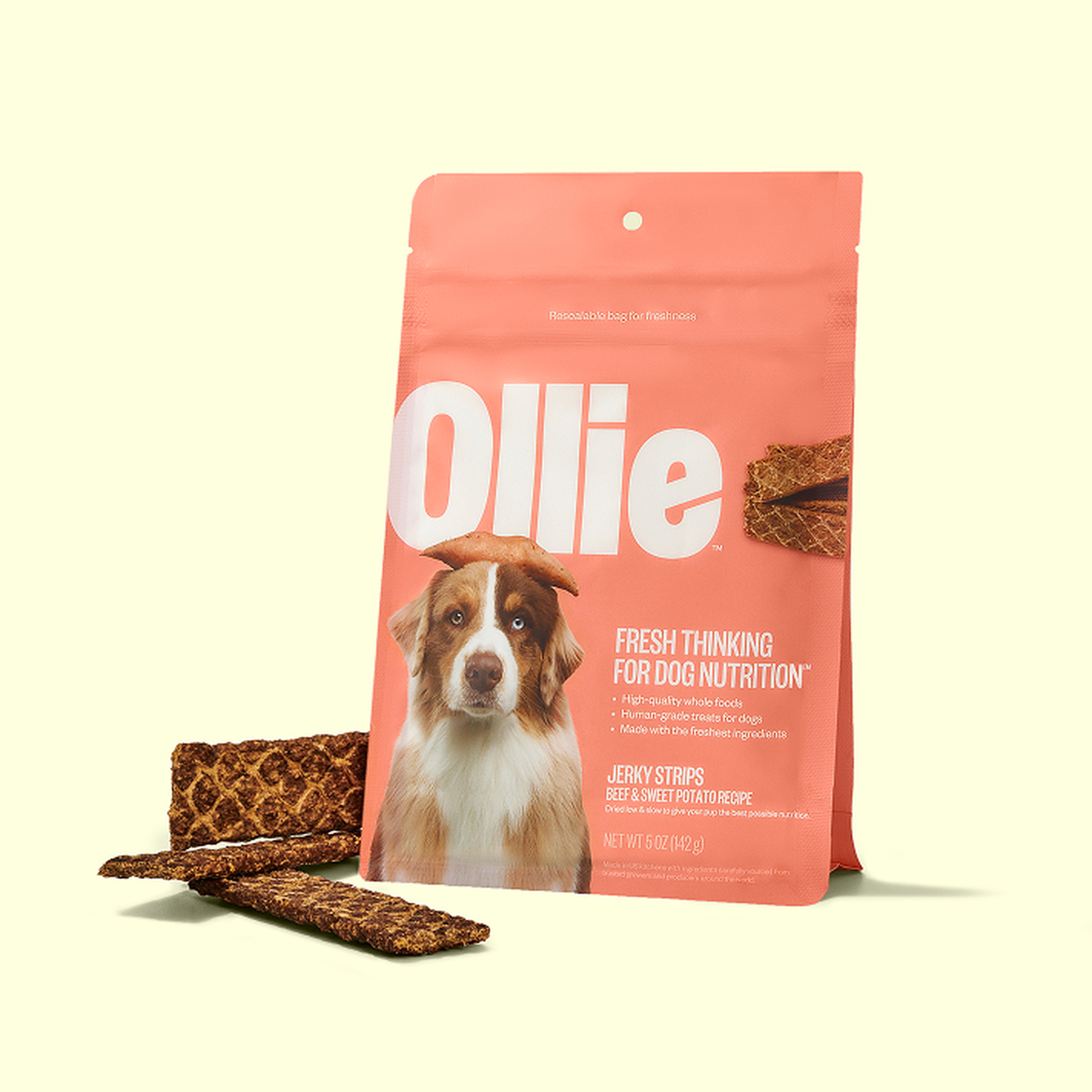 Pink package of Ollie dog jerky strips with an image of a dog, emphasizing fresh and high-quality ingredients. Jerky strips are placed beside the pack.
