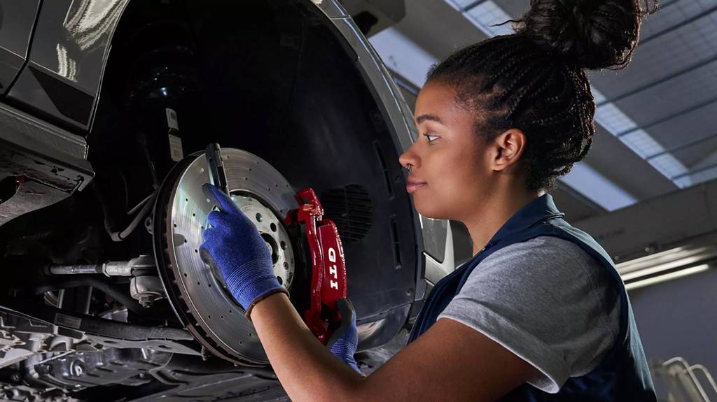 A woman working on a Volkswagen's brakes