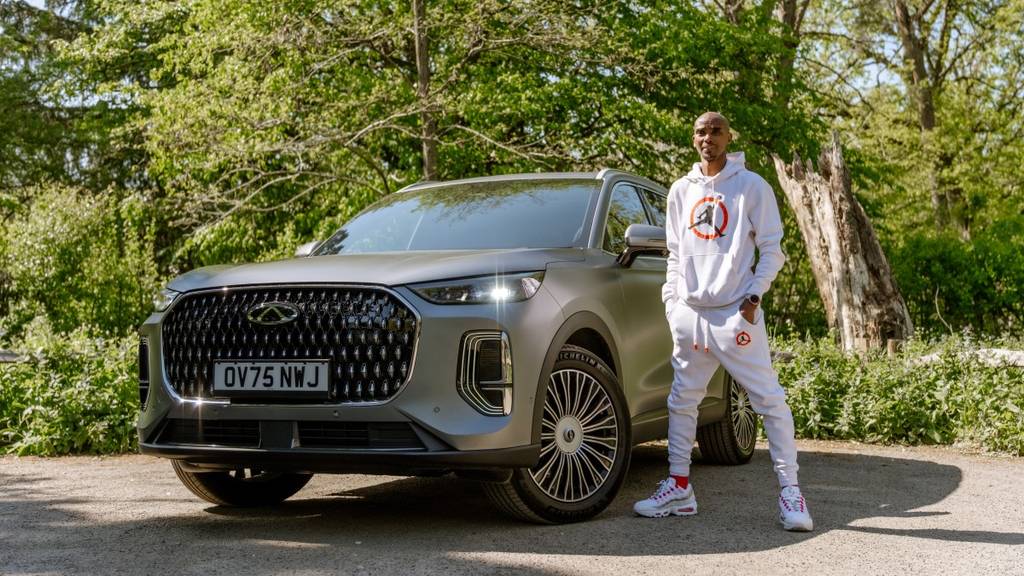 Sir Mo Farah standing beside a Chery TIGGO 9 Super Hybrid with a white tracksuit on and his hands in his pockets