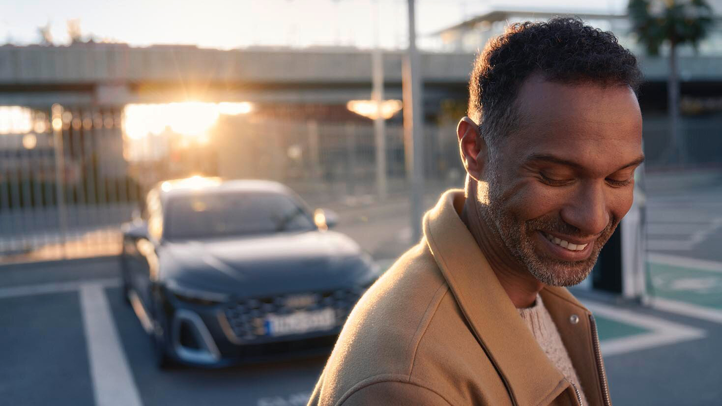 A man smiling in front of his Audi at sunset