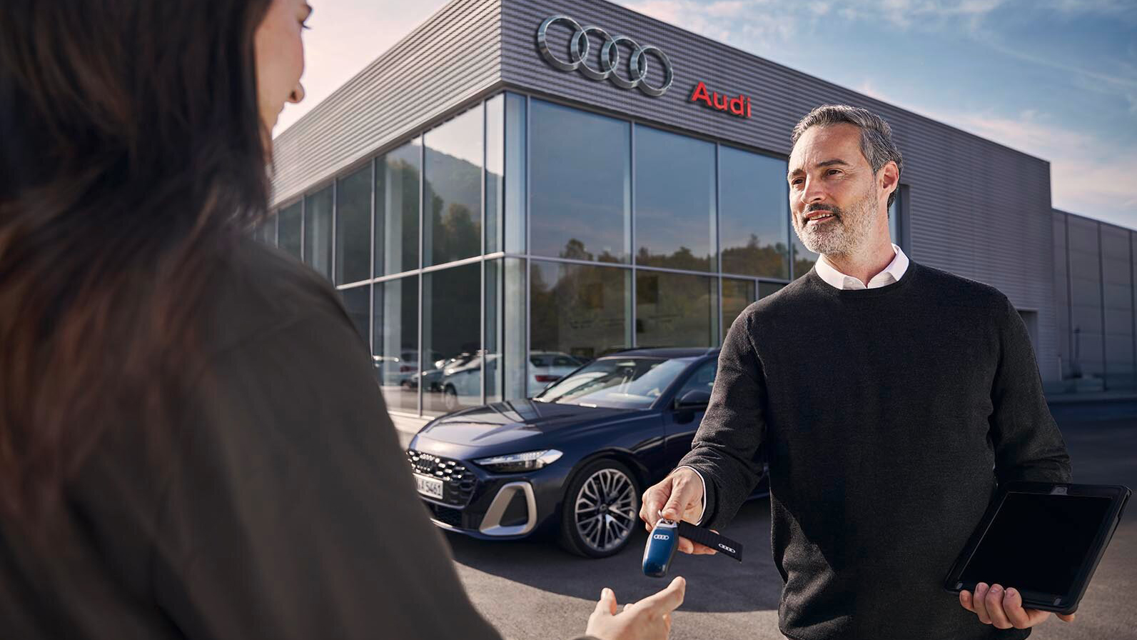 A man handing over keys to a woman outside a dealership