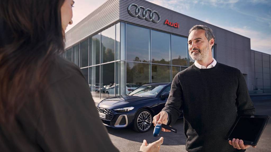 A man handing over keys to a woman outside a dealership