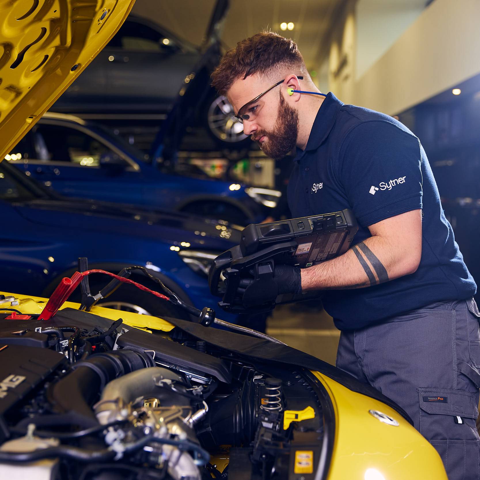 A technician working under the bonnet of a yellow car