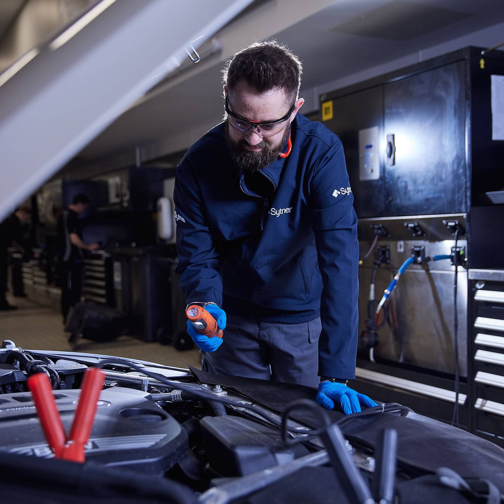 A technician looking under the bonnet of a grey car