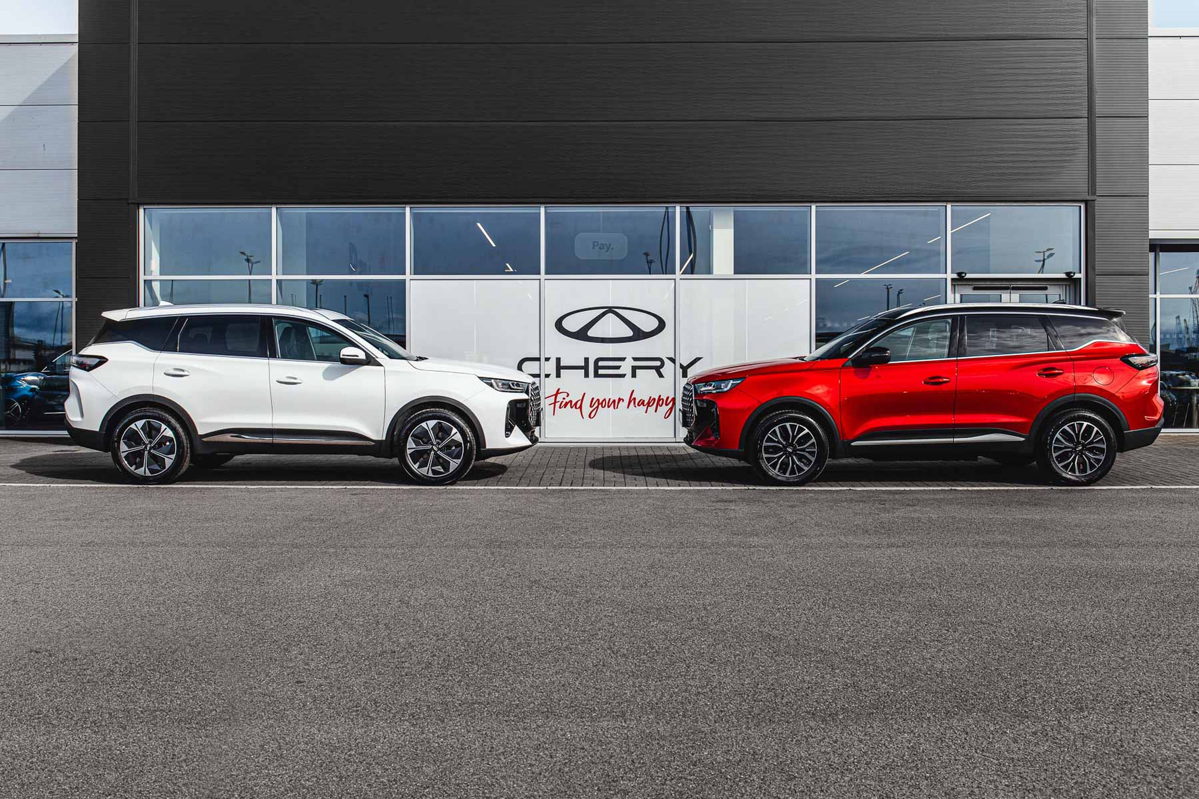 Two Chery TIGGO 7 SUVs, one white and one red, parked in front of a Chery dealership with large signage and glass windows.