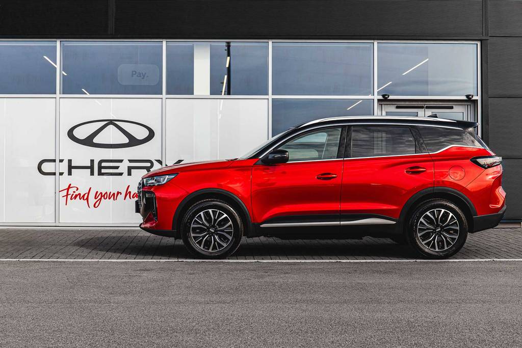 Chery TIGGO 7 SUV in red, parked in front of a Chery dealership with large signage and glass windows.