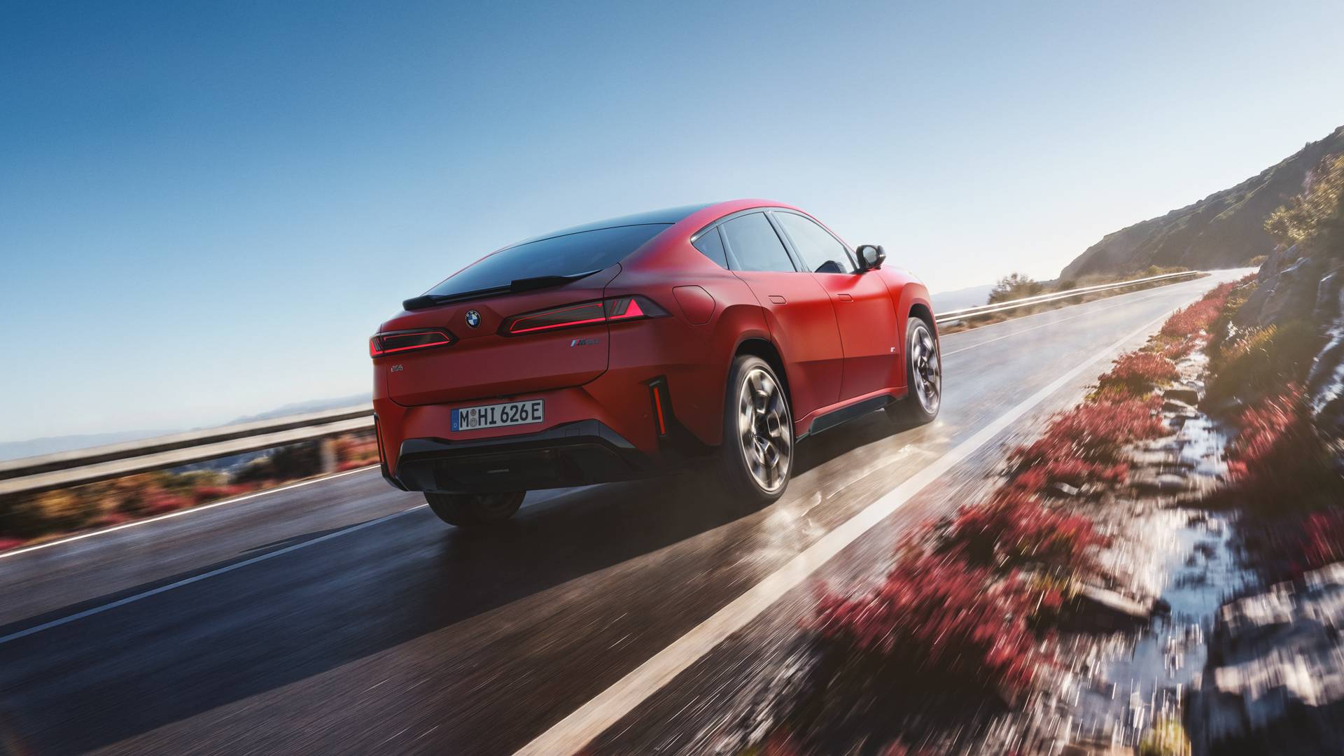 An AI generated image of a red BMW iX4 driving through a rain covered road along mountains, showcasing the back of the car