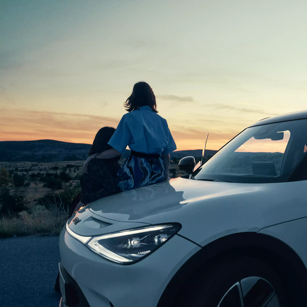 Two people sat on the bonnet of a new smart, looking into the distance