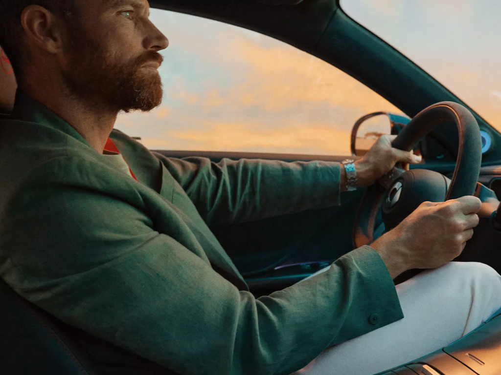 A bearded man driving his smart taken from the perspective of the passenger, with both hands on the wheel