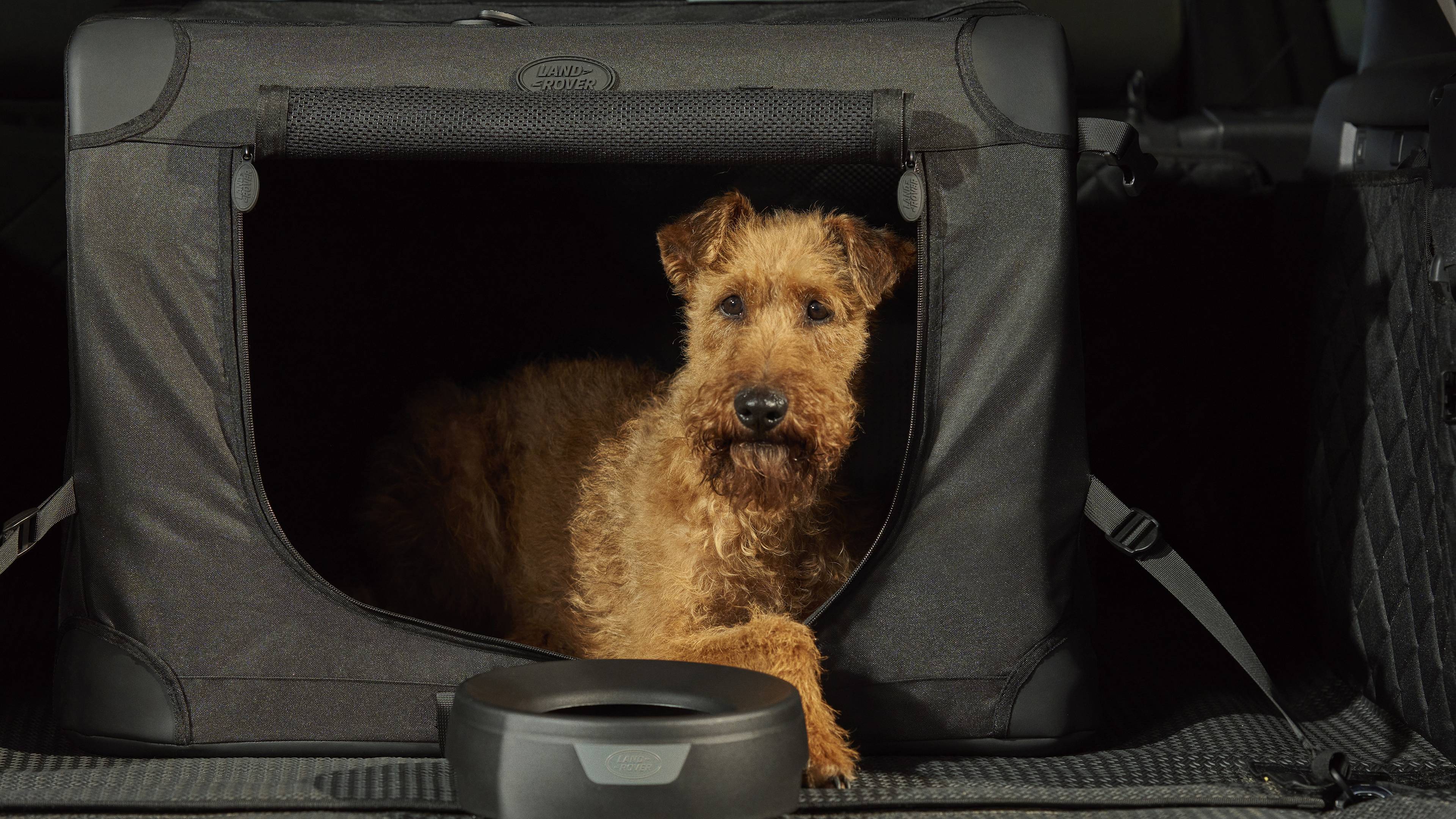 small brown dog sat inside a land rover branded pet accessory with a land rover water bowl infront