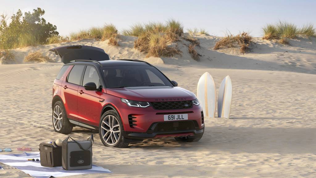 red discovery sport in sand with white surfboards and a blue blanket with land rover bags on top
