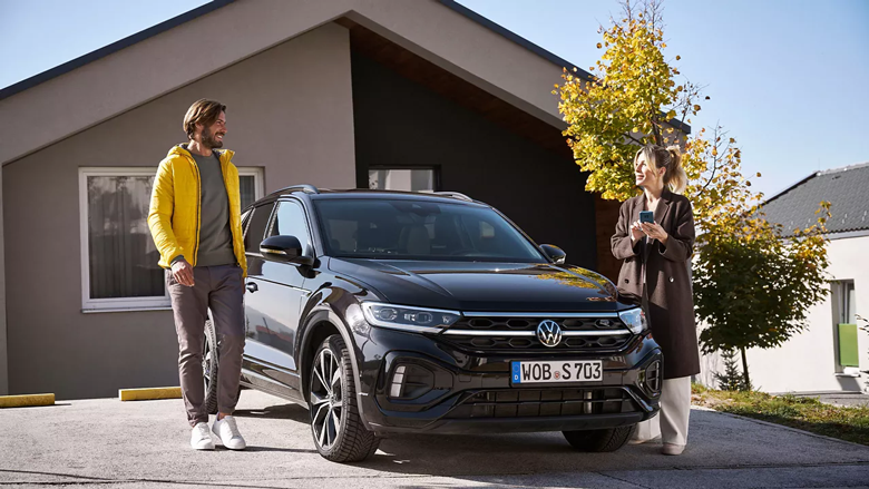A man and woman smiling beside a Volkswagen