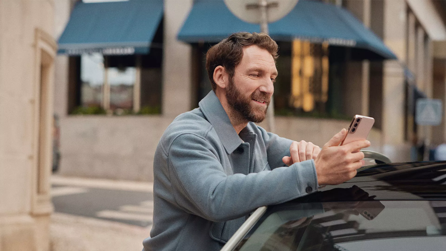 A man leaning over a Volkswagen looking at his phone