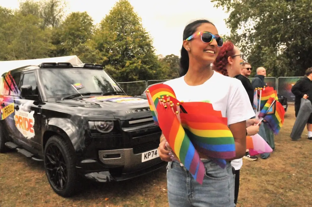 Someone stood in front of a Black Land Rover Defender holding multicoloured flags at Leicester Pride 2025