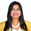 A woman with long black hair, smiling, wearing a yellow jacket, white top, and a pearl necklace against a white background.