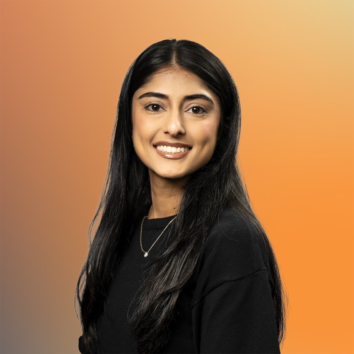 Smiling woman with long dark hair, wearing a black top and necklace, against a gradient orange background.