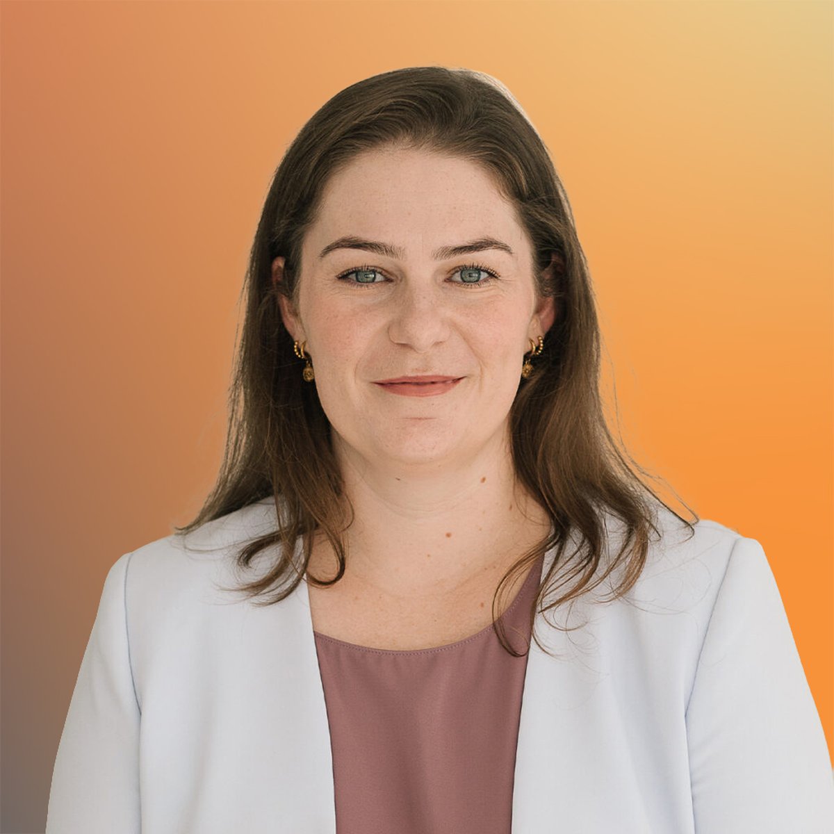 Woman with long brown hair wearing a white blazer and pink top, smiling with a soft orange gradient background.