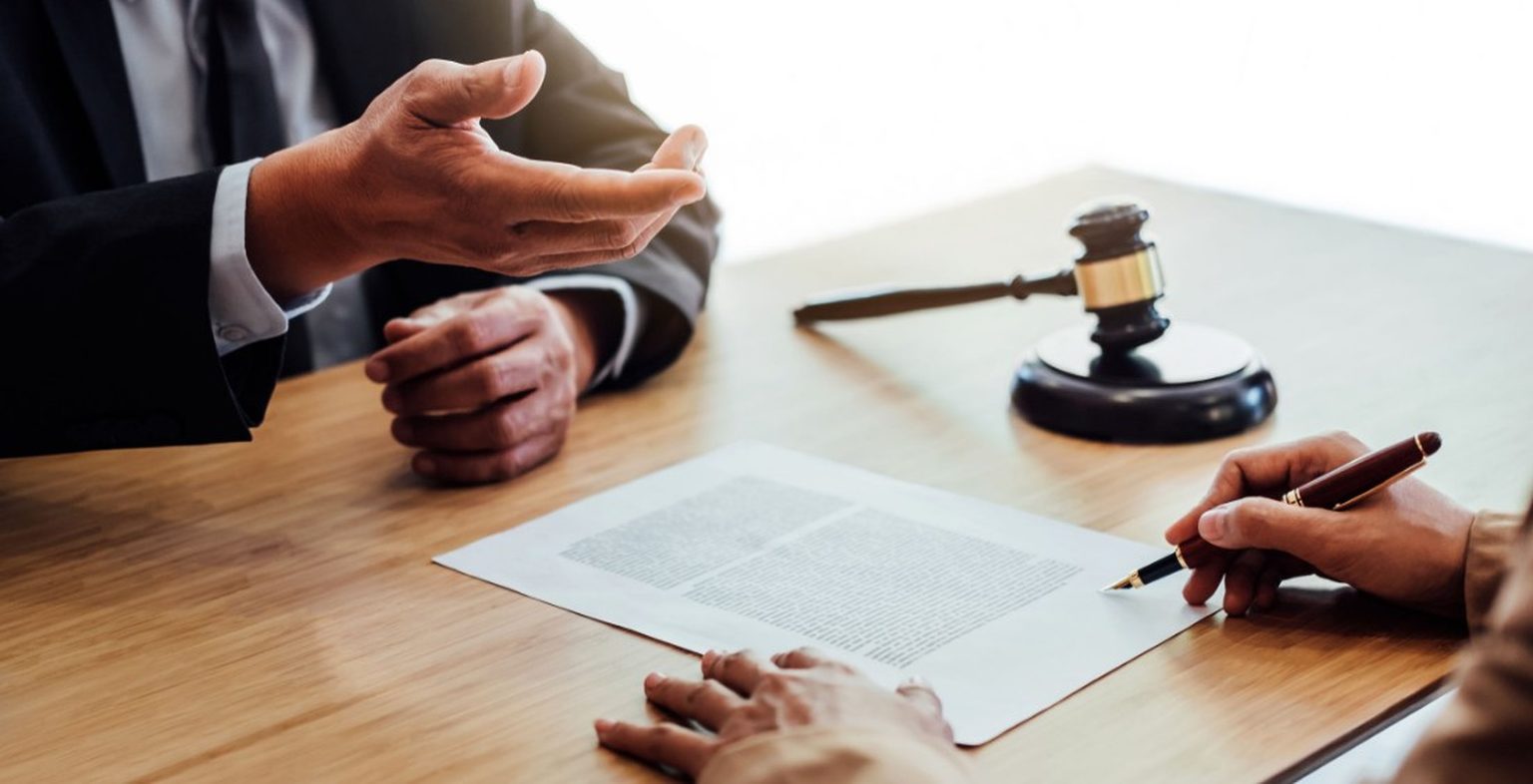 person signing a document at a desk with a lawyer 