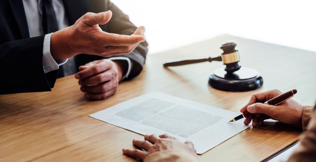 person signing a document at a desk with a lawyer 