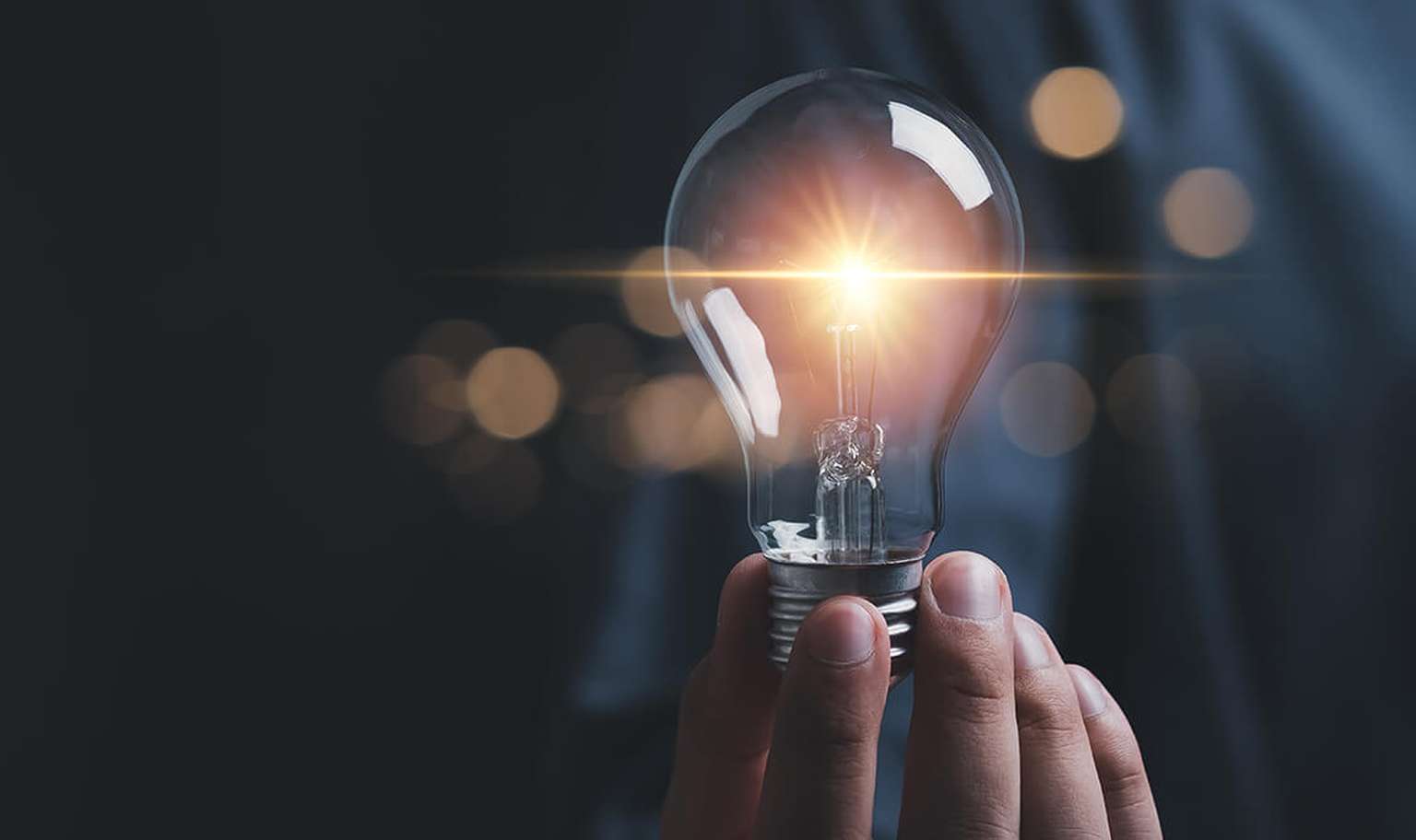 Hand holding a glowing light bulb against a dark background, symbolizing innovation and creativity.