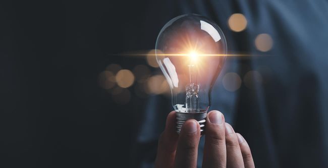 Hand holding a glowing light bulb against a dark background, symbolizing innovation and creativity.