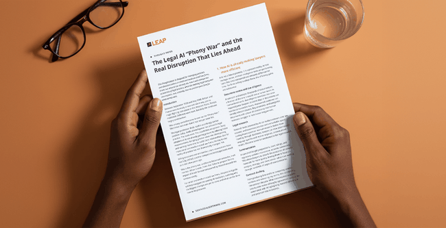 Hands holding a document titled "The Legal AI 'Phony War'" on a desk with a pair of glasses and a glass of water.