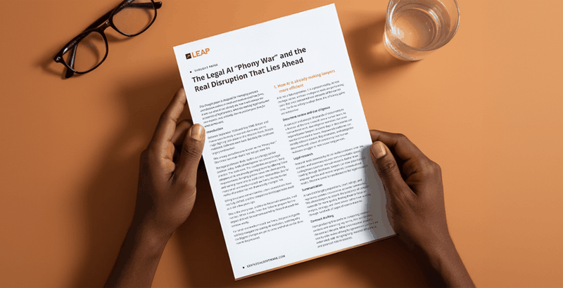 Hands holding a document titled "The Legal AI 'Phony War'" on a desk with a pair of glasses and a glass of water.