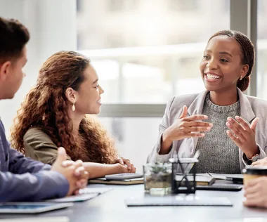 Four people having a lively discussion around a conference table, with one person actively speaking and others listening intently.