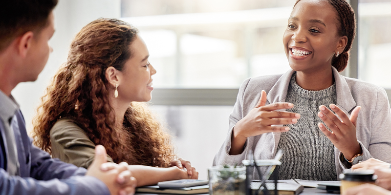 Four people having a lively discussion around a conference table, with one person actively speaking and others listening intently.