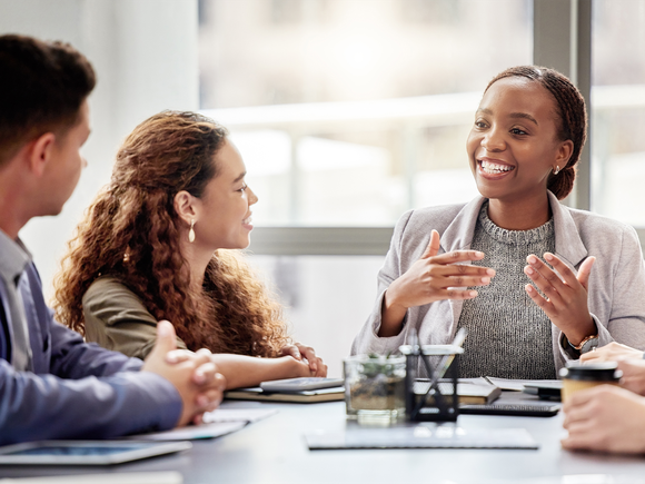 Four people having a lively discussion around a conference table, with one person actively speaking and others listening intently.