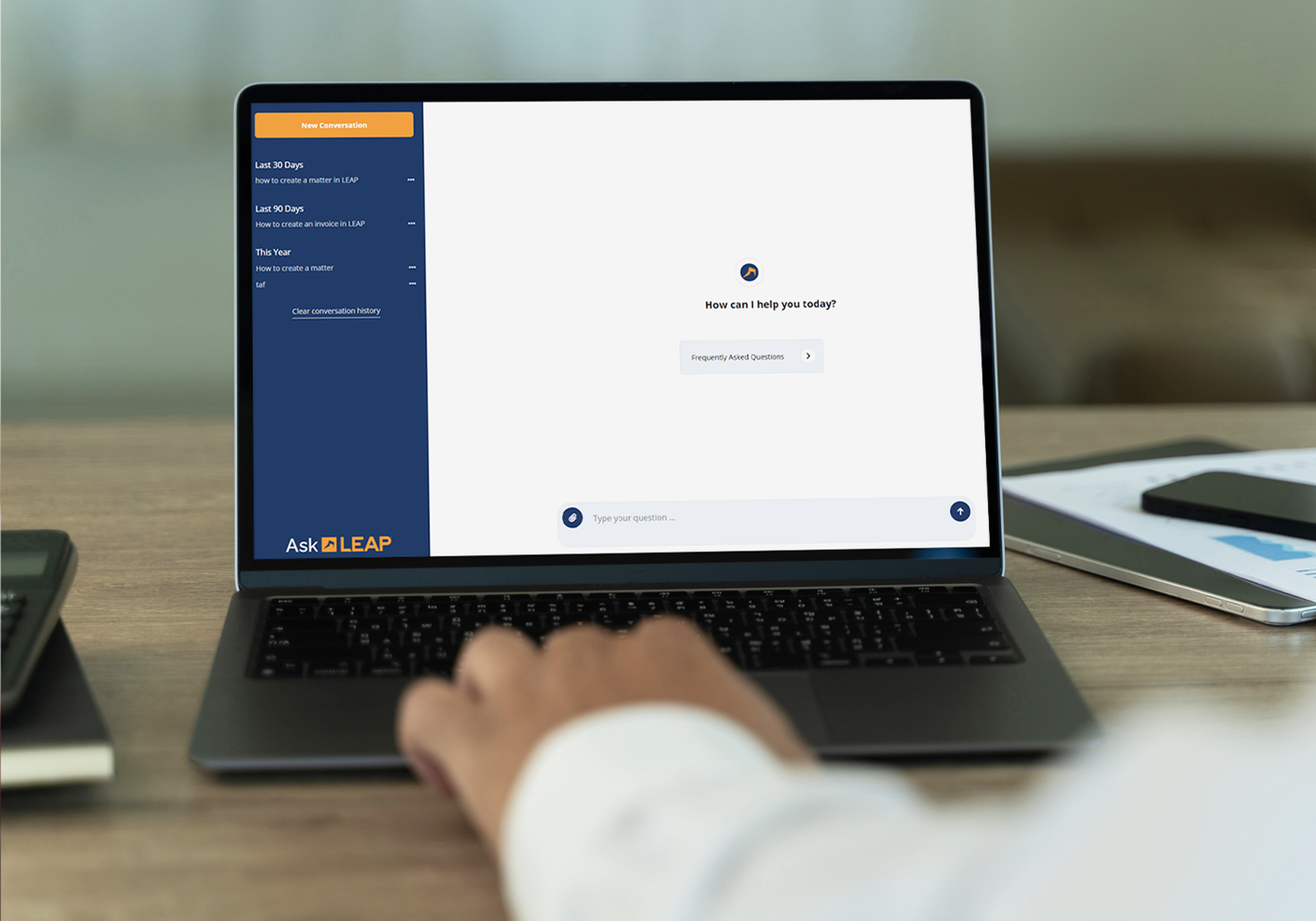 Person using a laptop displaying a chatbot interface with "How can I help you today?" on the screen, in a modern office setting.
