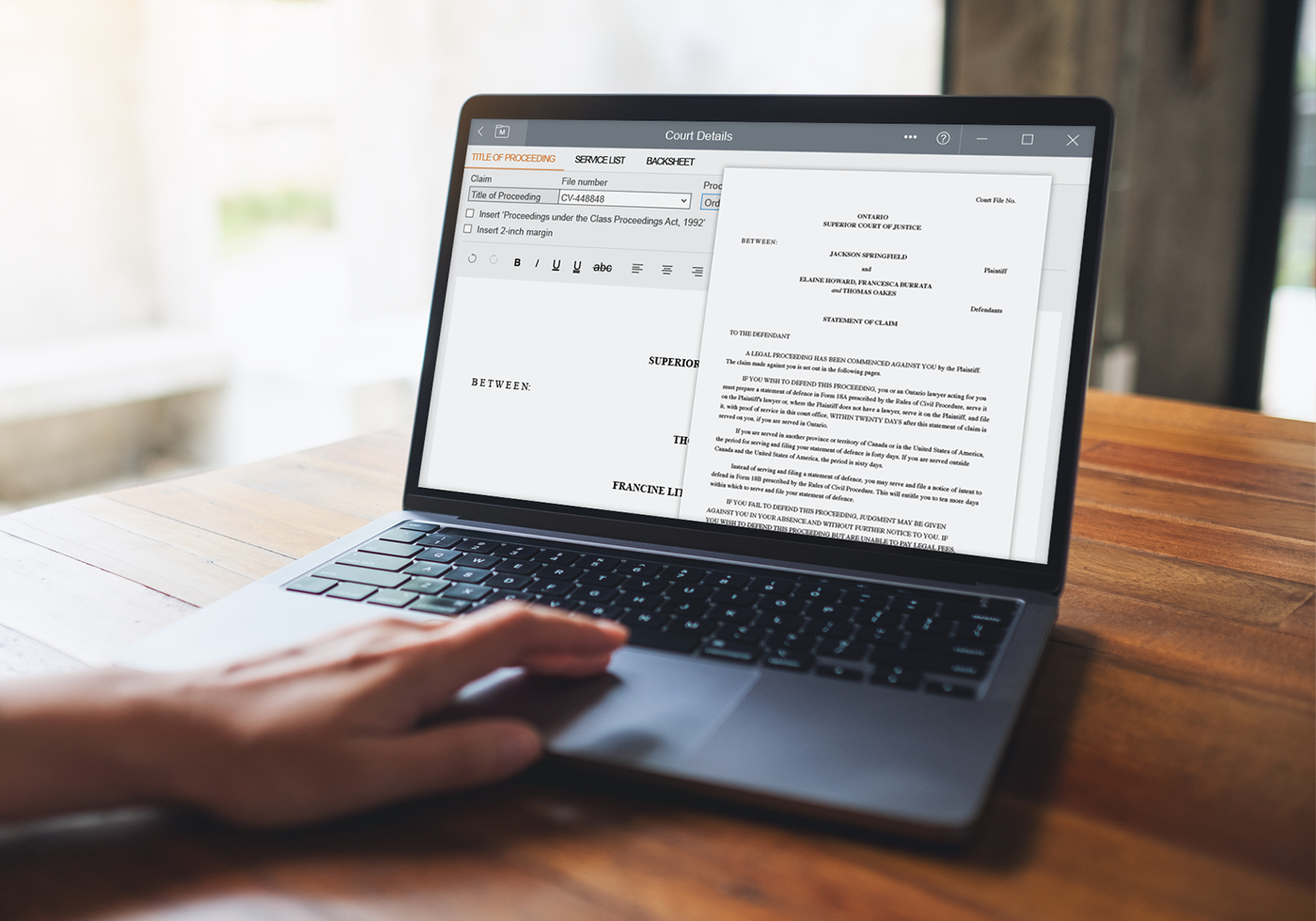 A person uses a laptop displaying a legal document with text and form fields, on a wooden table in a well-lit room.
