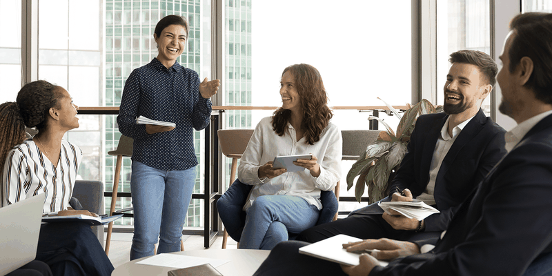 A diverse group of professionals, seated in a modern office setting, engaged in a lively and casual discussion.