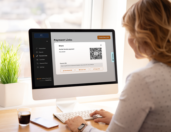 Woman using a computer displaying a payment link page with a QR code, surrounded by a coffee cup and a bright window in the background.