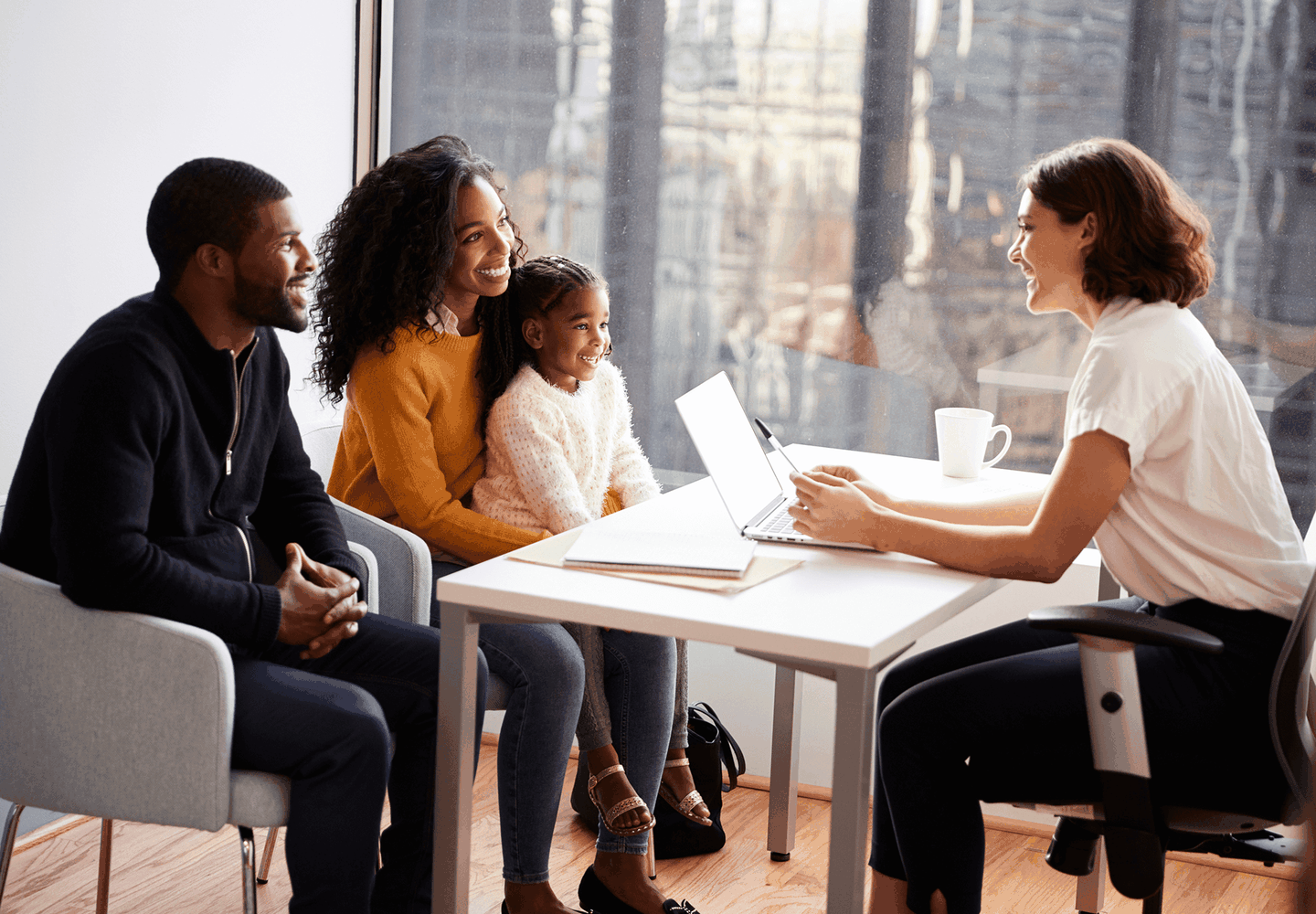 A family of three sits across from a professional woman in an office. They are smiling and engaged in discussion.