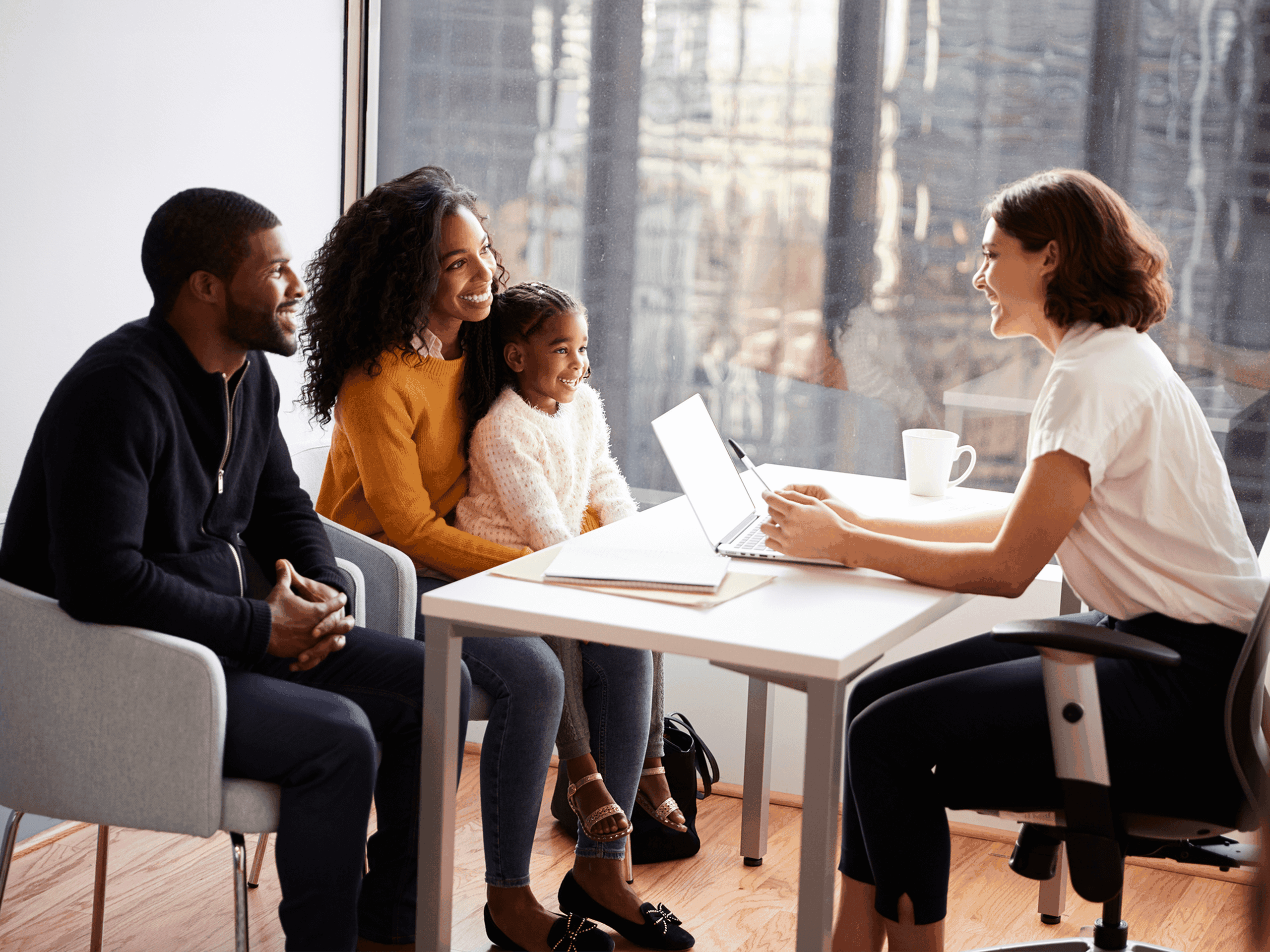 A family of three sits across from a professional woman in an office. They are smiling and engaged in discussion.