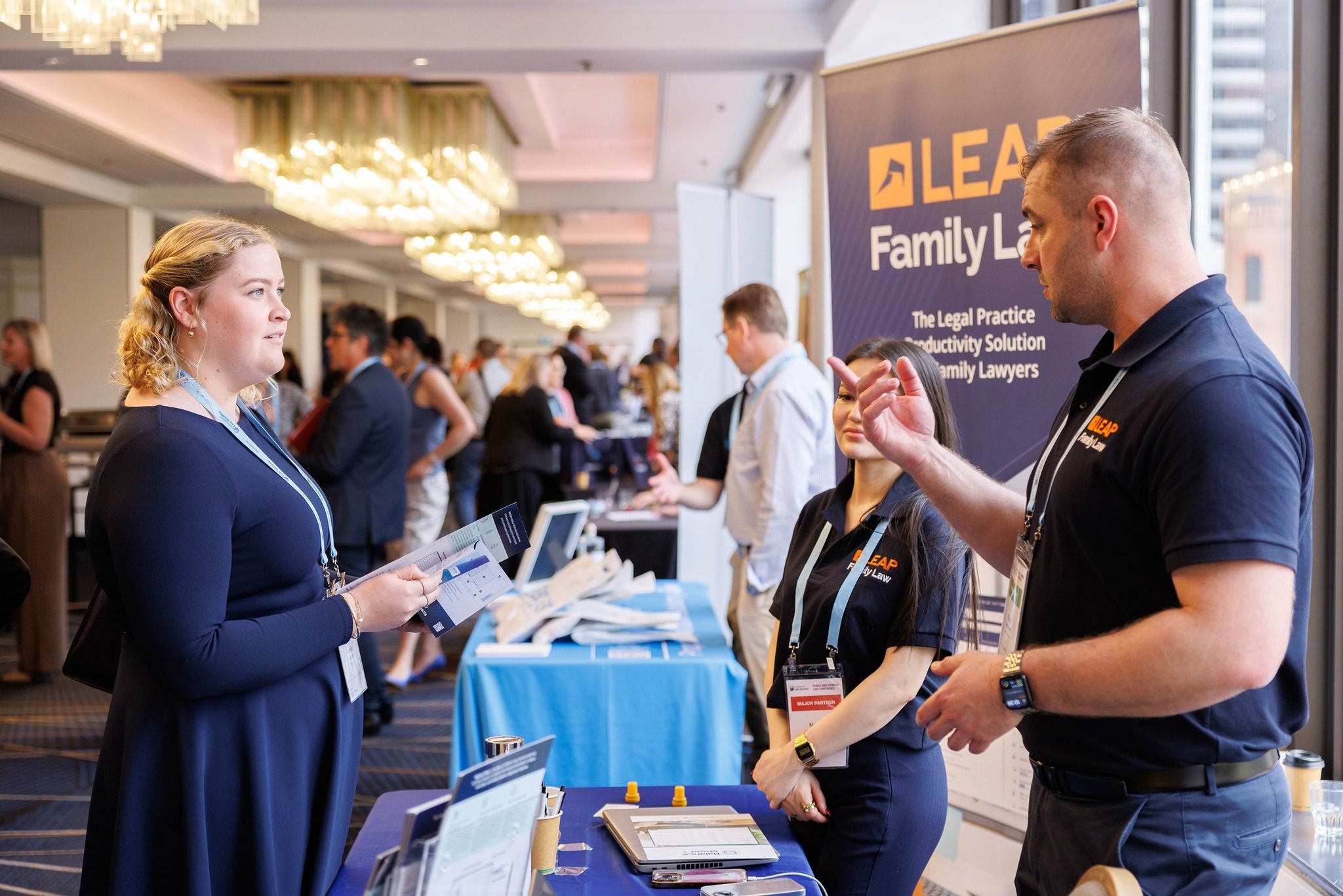 People at a business expo booth, engaging in conversation, with a banner in the background promoting legal practice solutions.